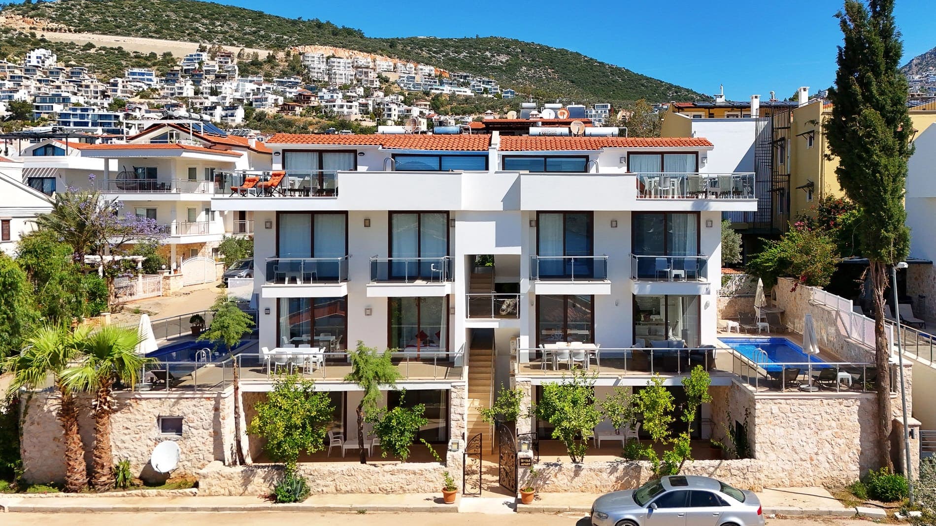 Çok katlı beyaz apart villanın ön cephesi, terasları ve havuz alanı.