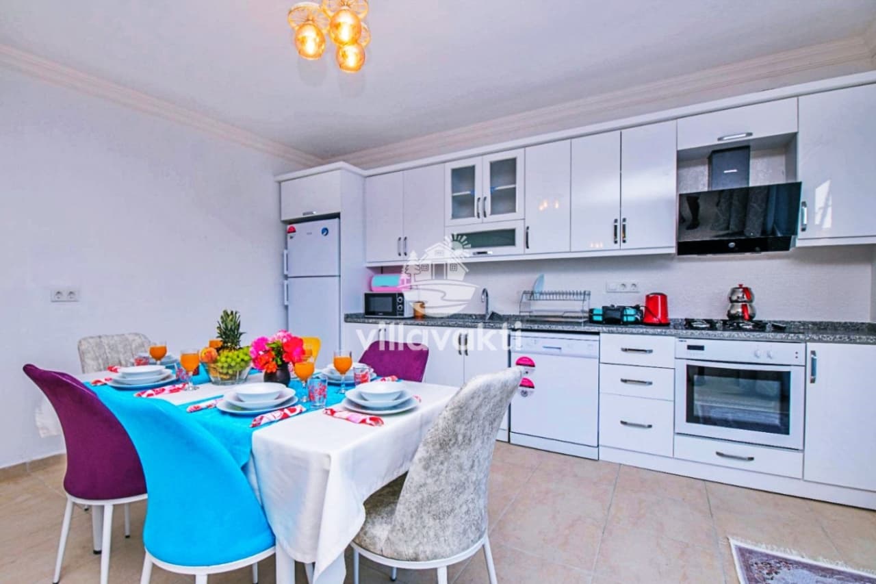 Beyaz mutfak dolapları ve yemek masası takımı bulunan iç mekân.