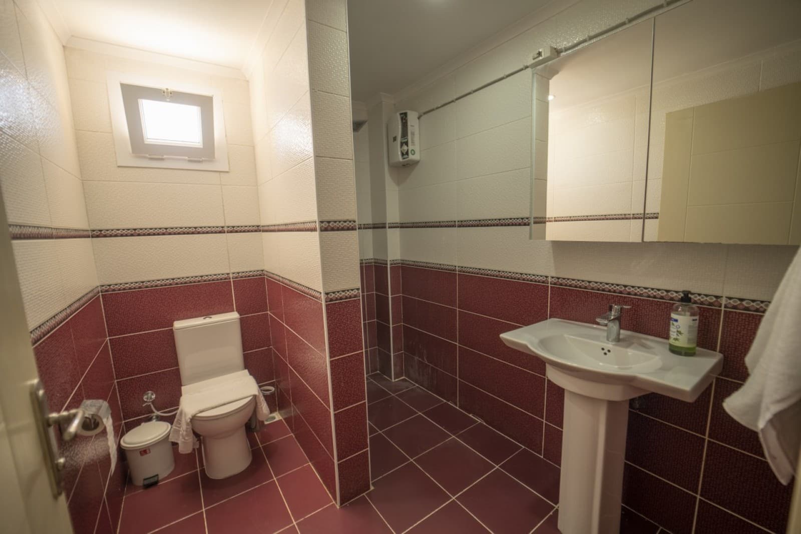 Bordo ve beyaz fayanslı banyoda klozet ve ayaklı lavabo yer alıyor.