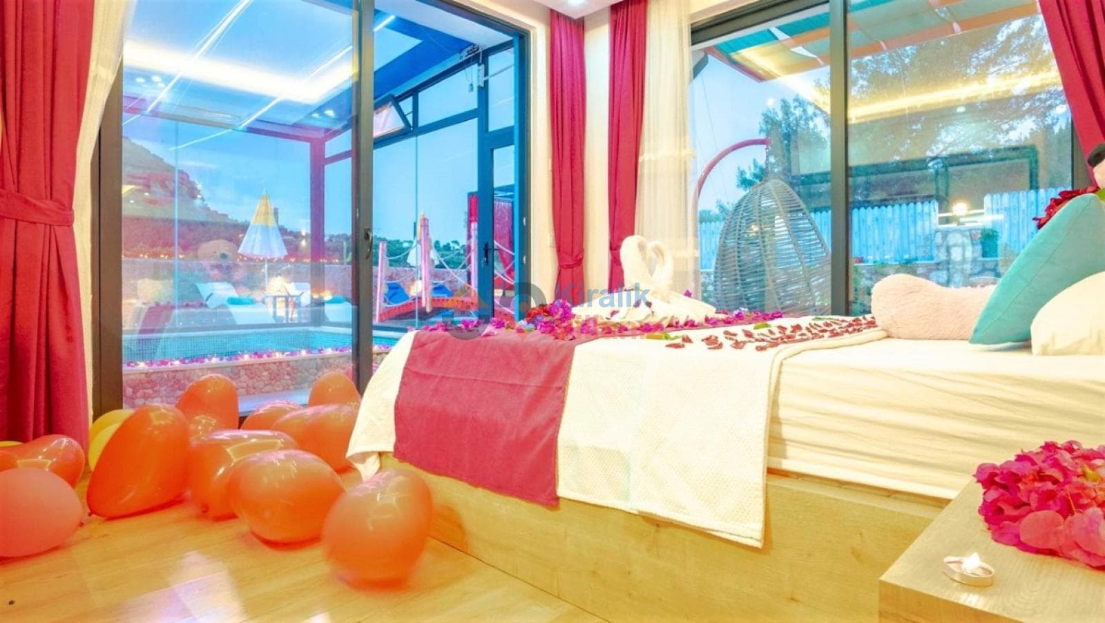 Yatak üzerinde balonlar ve çiçeklerle süslenmiş, havuz manzaralı cam duvarlı yatak odası.