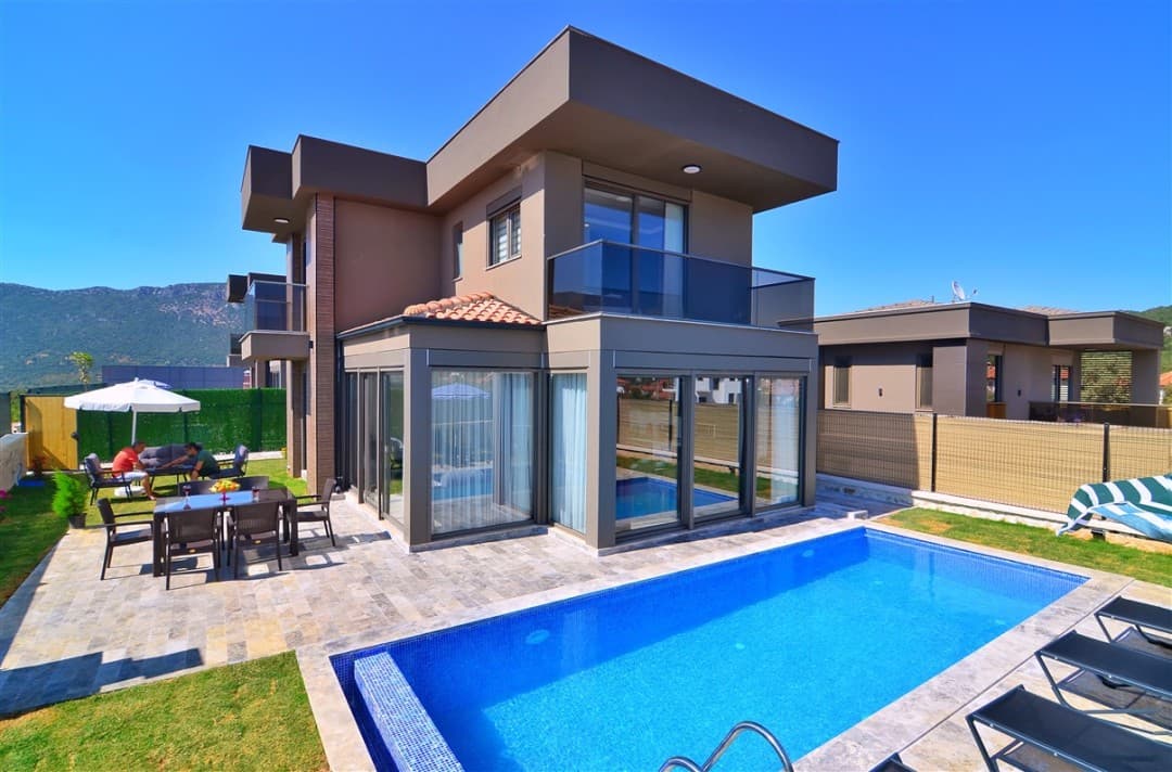 Mavi havuzlu, bahçesinde yemek masası ve oturma grubu bulunan modern mimarili iki katlı villa.