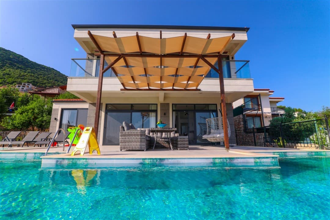 Önünde havuz ve veranda tenteli oturma grubu olan iki katlı villa.