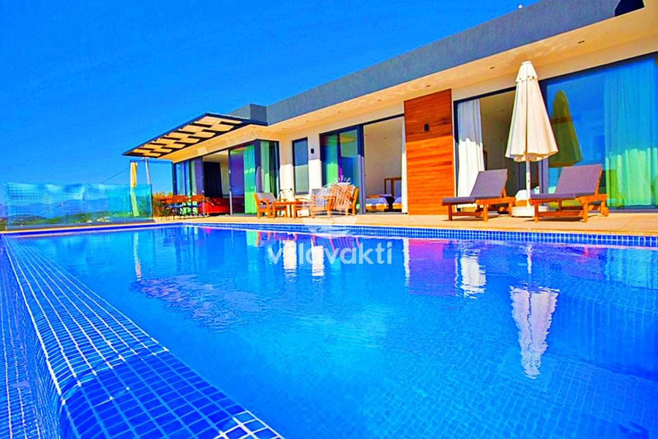 Geniş yüzme havuzu ve şezlonglar bulunan modern villa dış mekanı.