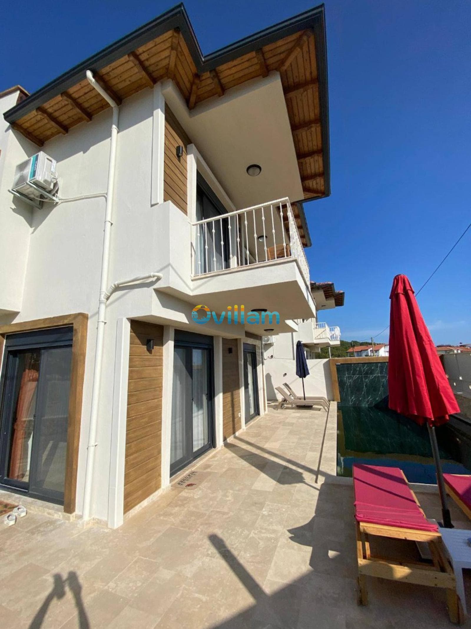 Balkonlu ve havuz kenarında şezlonglar bulunan beyaz villa dış cephesi.
