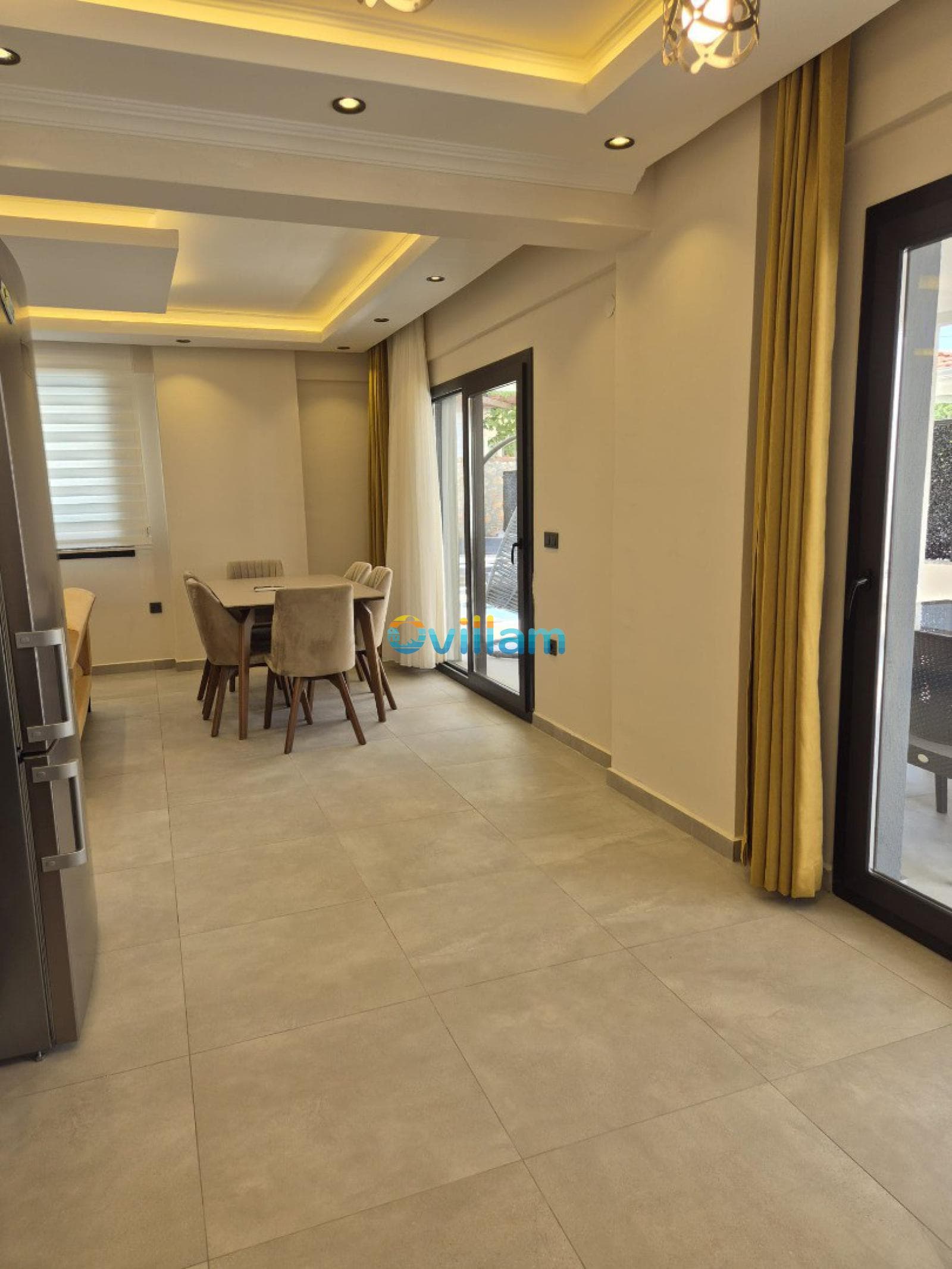 Modern aydınlatmalı, bej sandalyeli yemek masası bulunan sade bir iç mekân.