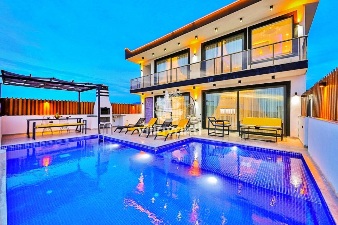 İki katlı modern villanın havuzu, şezlongları ve akşam ışıklarıyla aydınlatılmış terası.