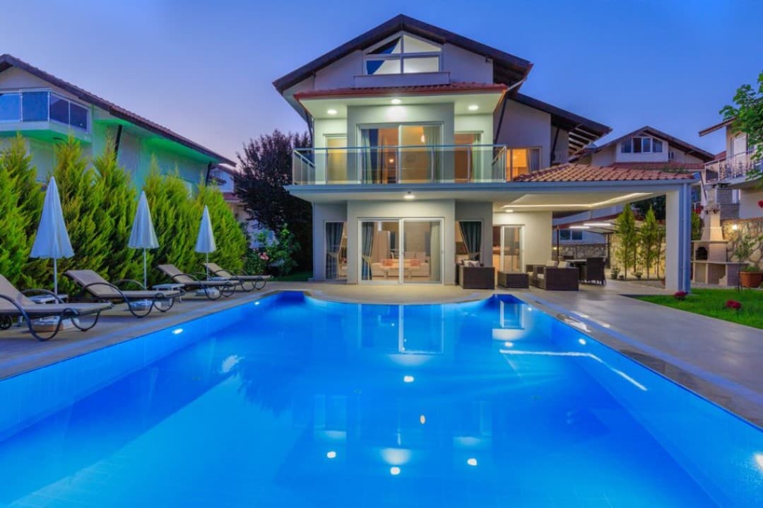 Akşam saatinde havuzu ve şezlongları olan aydınlatılmış müstakil villa.