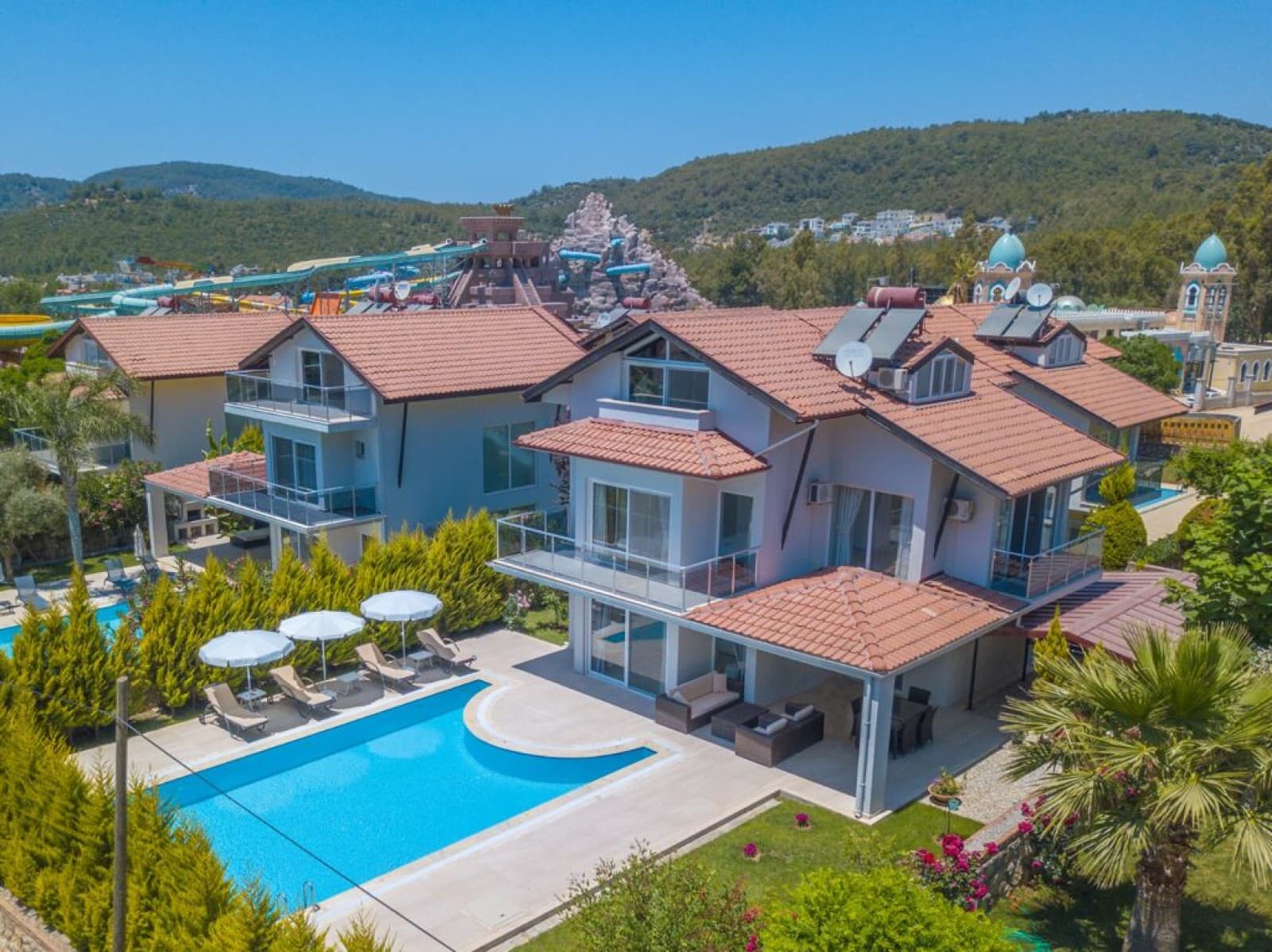 Ağaçlar arasında havuzlu iki katlı kiremit çatılı villanın dış cephesi.