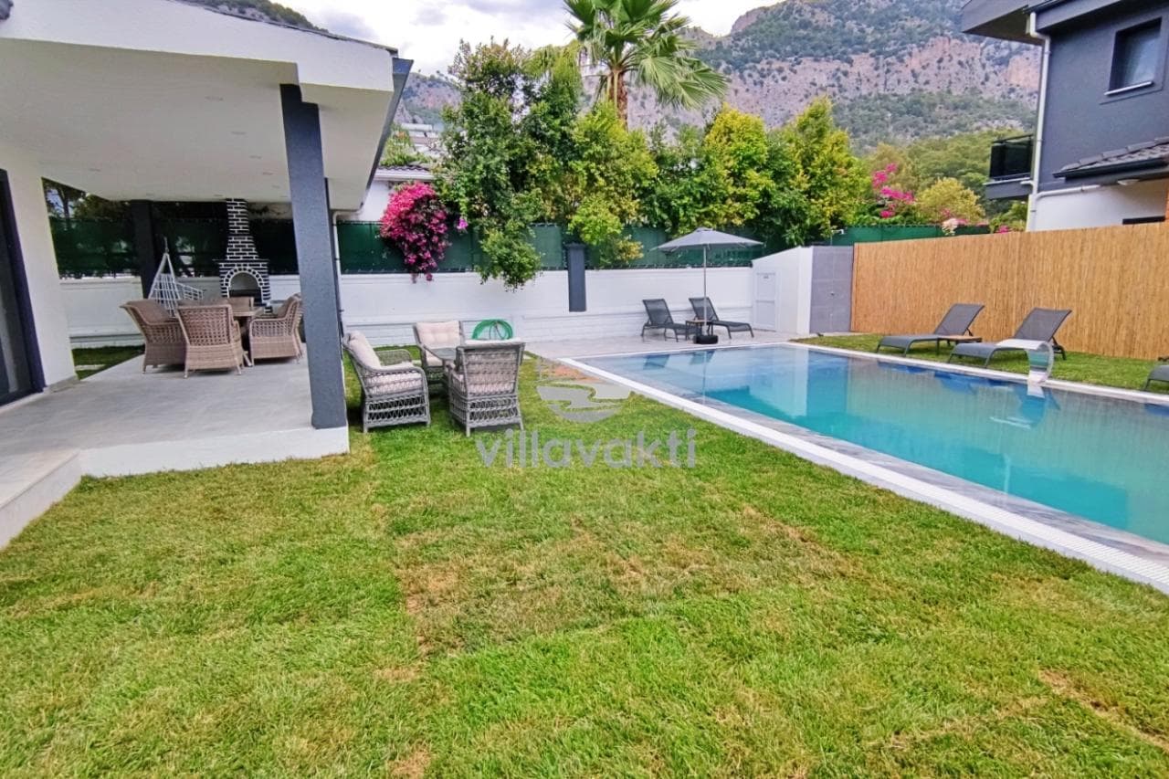 Özel yüzme havuzu, şezlonglar, yemek masası ve dış mekân oturma grubu bulunan villa bahçesi.