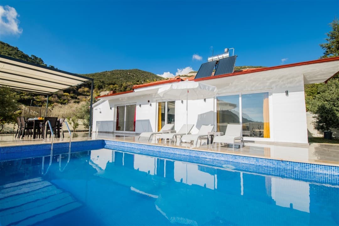 Mavi havuzun başında şezlonglar ve arka planda beyaz tek katlı villa.