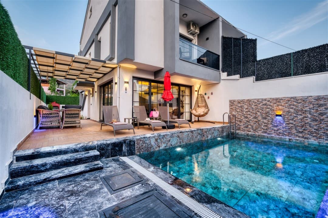 Önünde havuzu, şezlongları ve oturma alanı olan iki katlı modern villa.