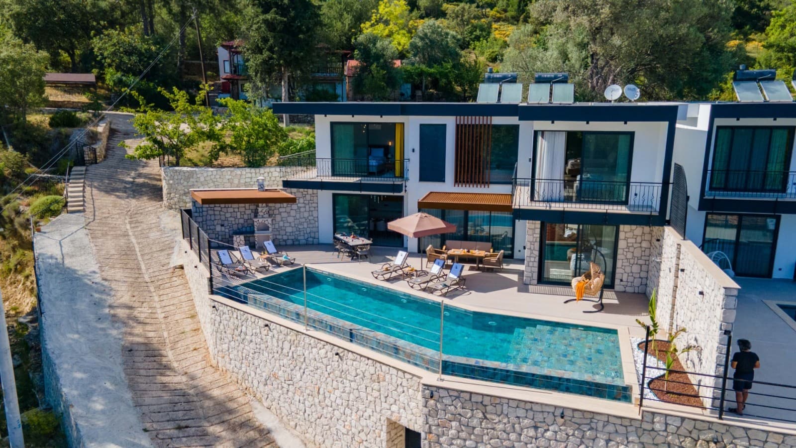 Önünde uzun havuzu ve şezlongları bulunan iki katlı taş kaplamalı villa.