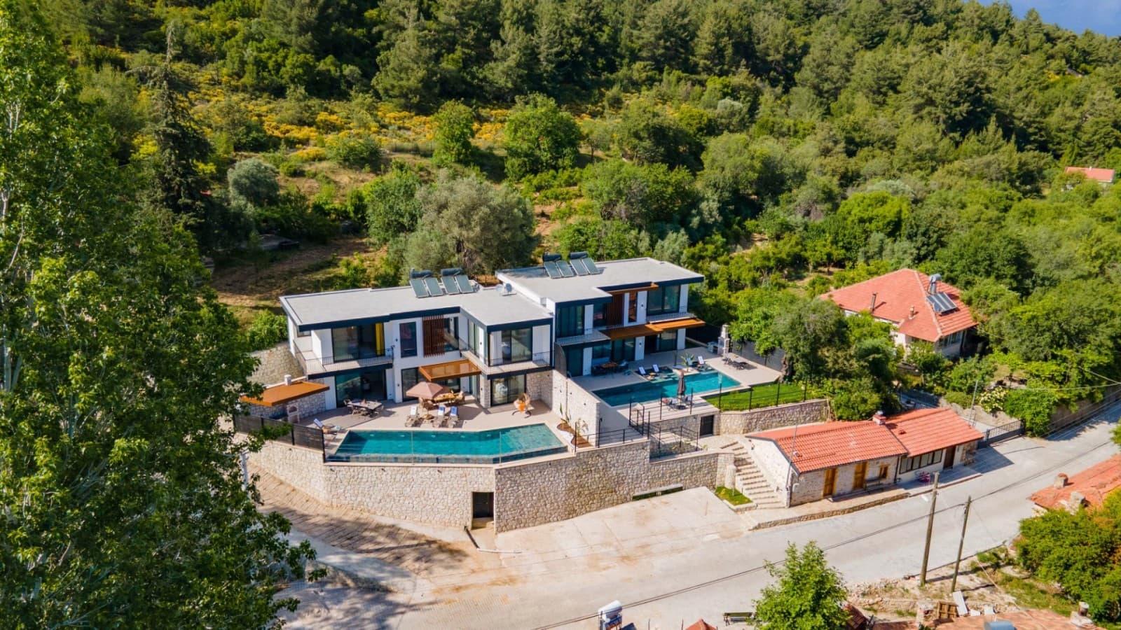 Orman içinde iki havuzlu modern lüks villanın havadan görünümü.