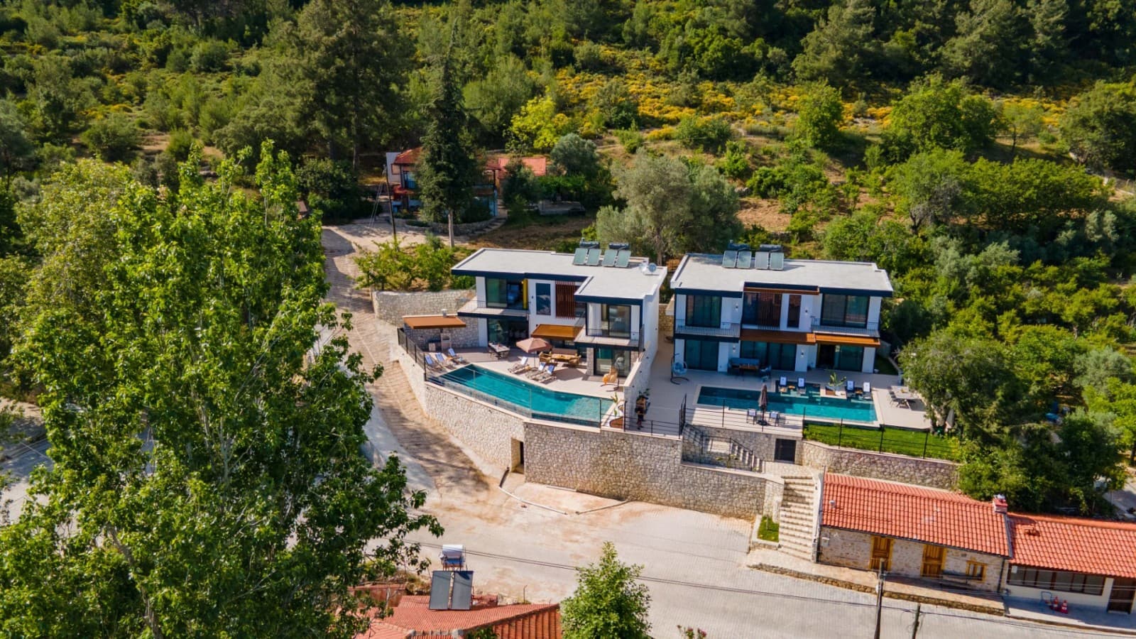 Yeşillikler içindeki yamaçta yer alan havuzlu modern villaların havadan görünümü.