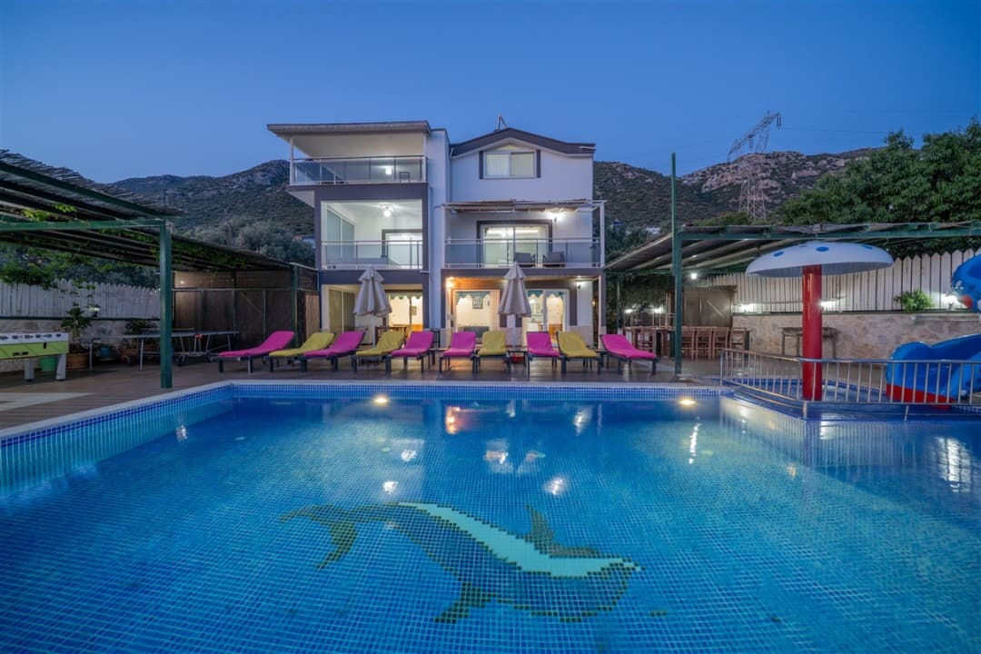 Akşam saatinde havuz başında şezlonglar olan iki katlı müstakil villa.