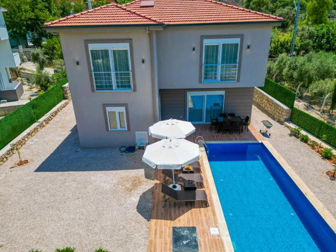Bahçesinde havuzu, şezlongları ve yemek masası bulunan iki katlı müstakil villa.