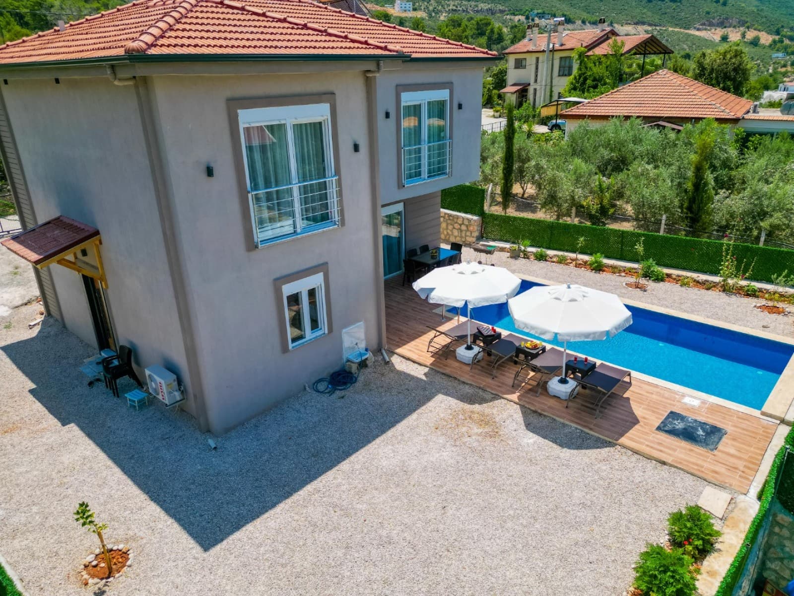 İki katlı bej villa, bahçesinde havuz ve şezlonglar.