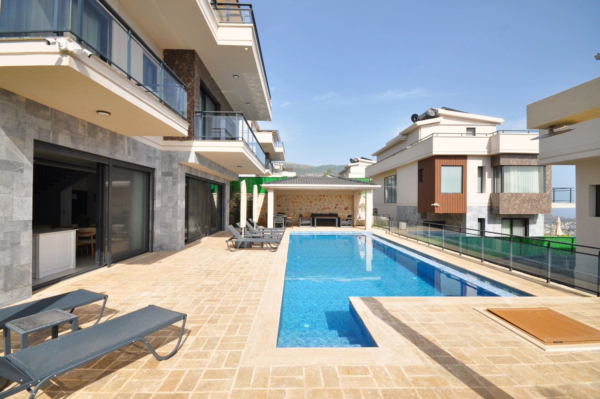Geniş havuz terası, şezlonglar ve modern mimarili çok katlı villa binaları.