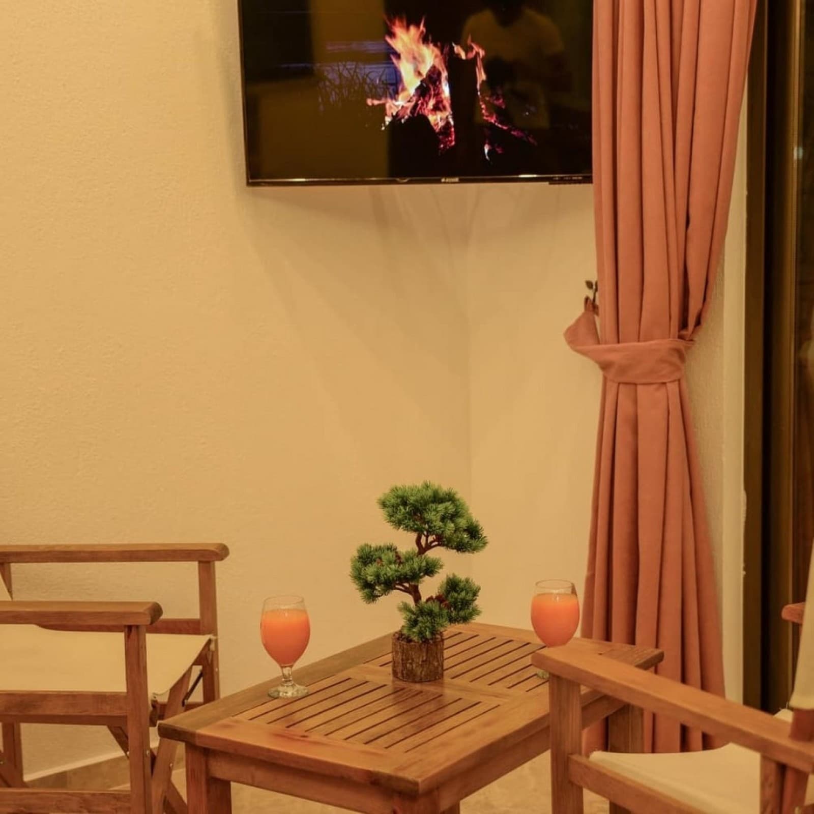 Ahşap sehpada iki bardak meyve suyu ve saksıda bonsai ağacı bulunuyor.