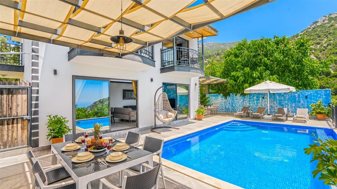 Güneşlikli havuz kenarında yemek masası ve salıncak bulunan beyaz villa.