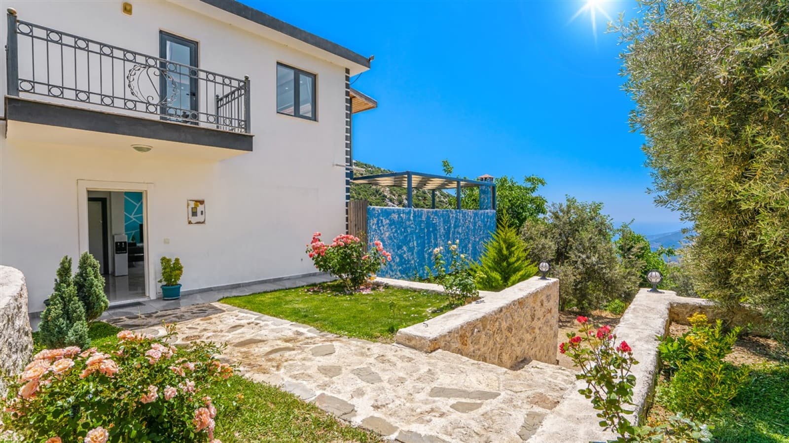 Taş merdivenli giriş yolu ve pembe çiçeklerin bulunduğu iki katlı beyaz villa.