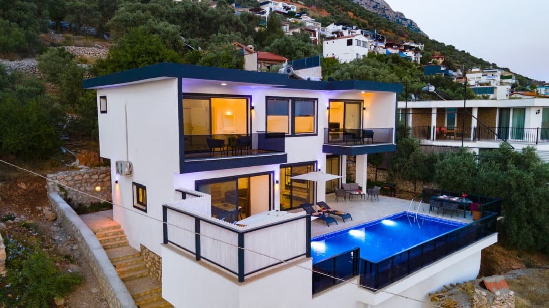 Akşam ışıklandırmalı, özel havuzlu, balkonlu ve modern mimariye sahip iki katlı beyaz villa.