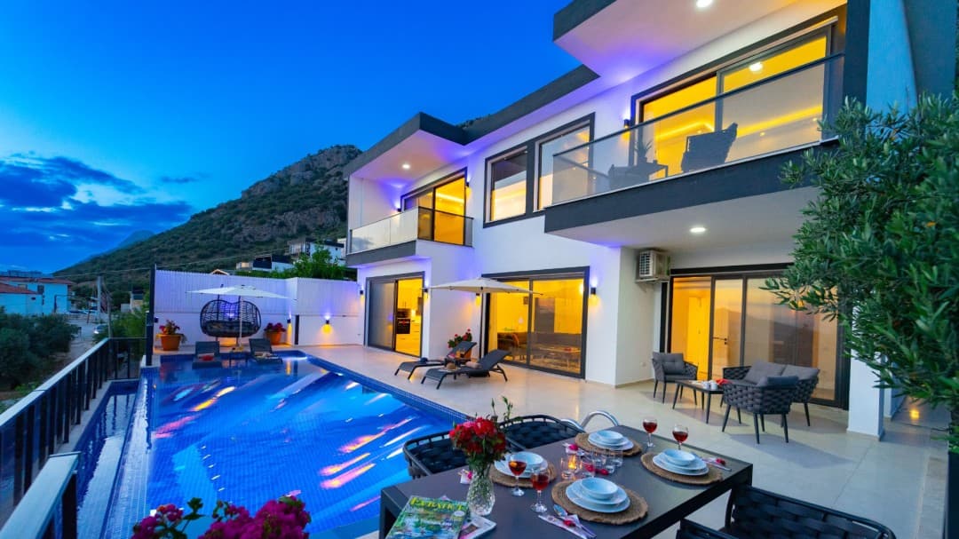Alacakaranlıkta havuzu, şezlongları ve yemek masası olan iki katlı modern villa.