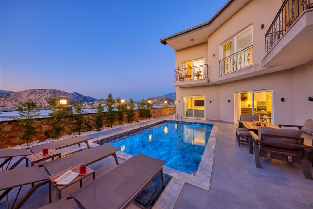 Akşam vakti havuz başı şezlongları ve dağ manzaralı iki katlı villa.