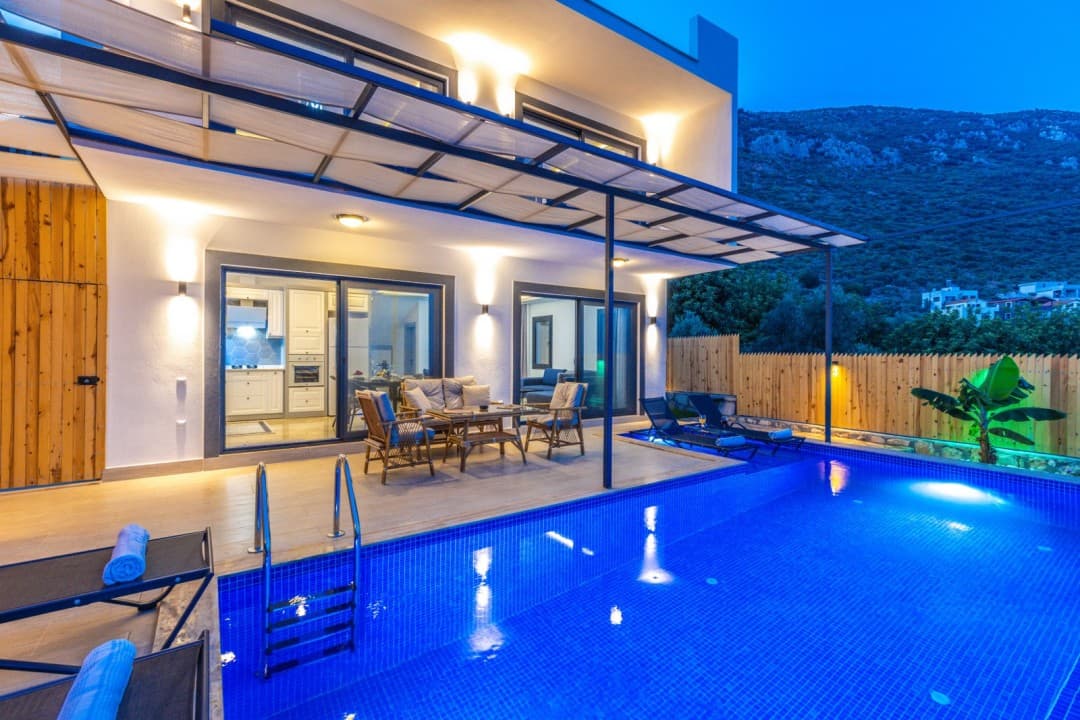 Akşam vakti aydınlatılmış havuzlu ve verandalı lüks villanın dış görünümü.