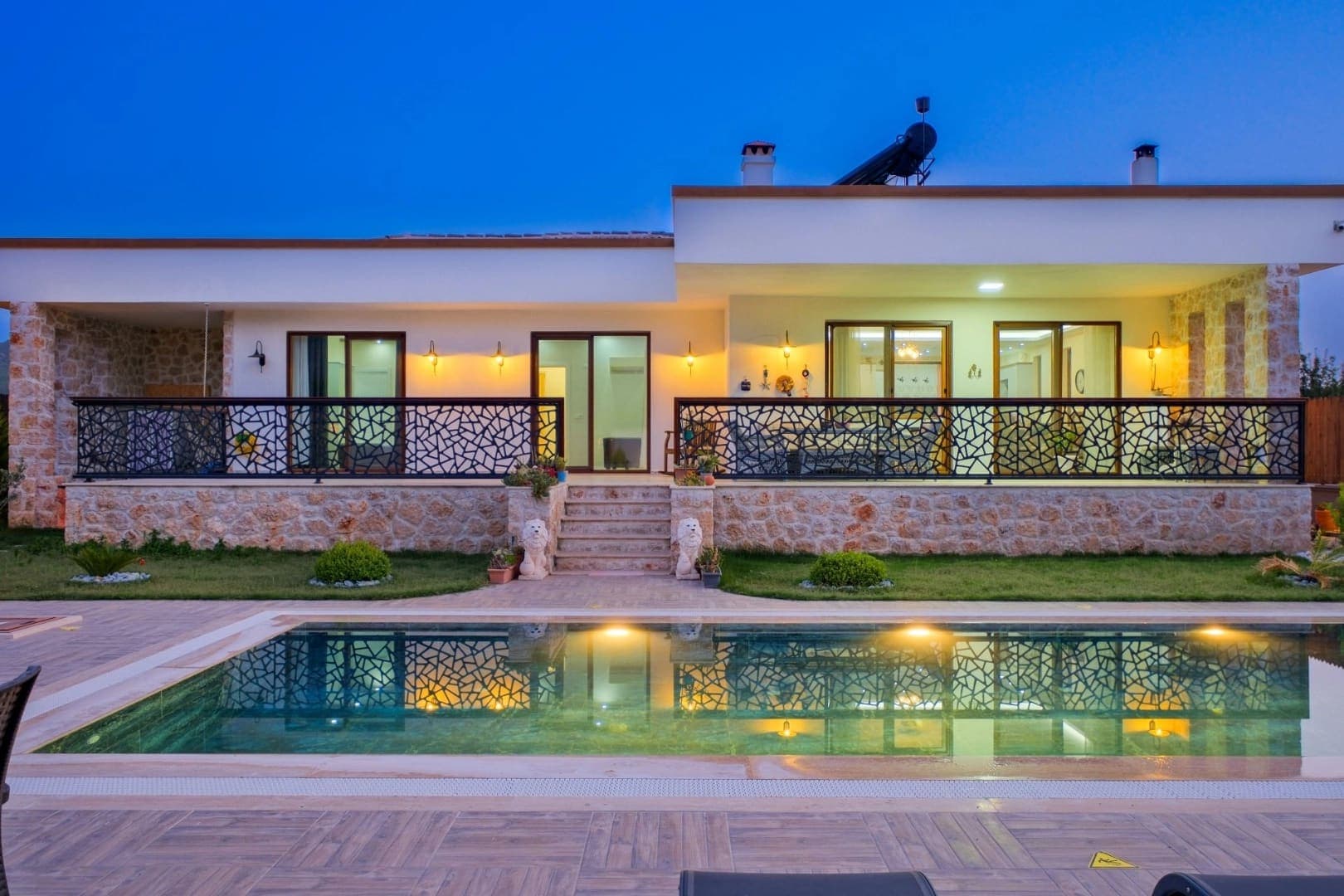 Akşam ışıklandırmalı, taş kaplama dış cepheye ve önünde havuz bulunan modern villa.