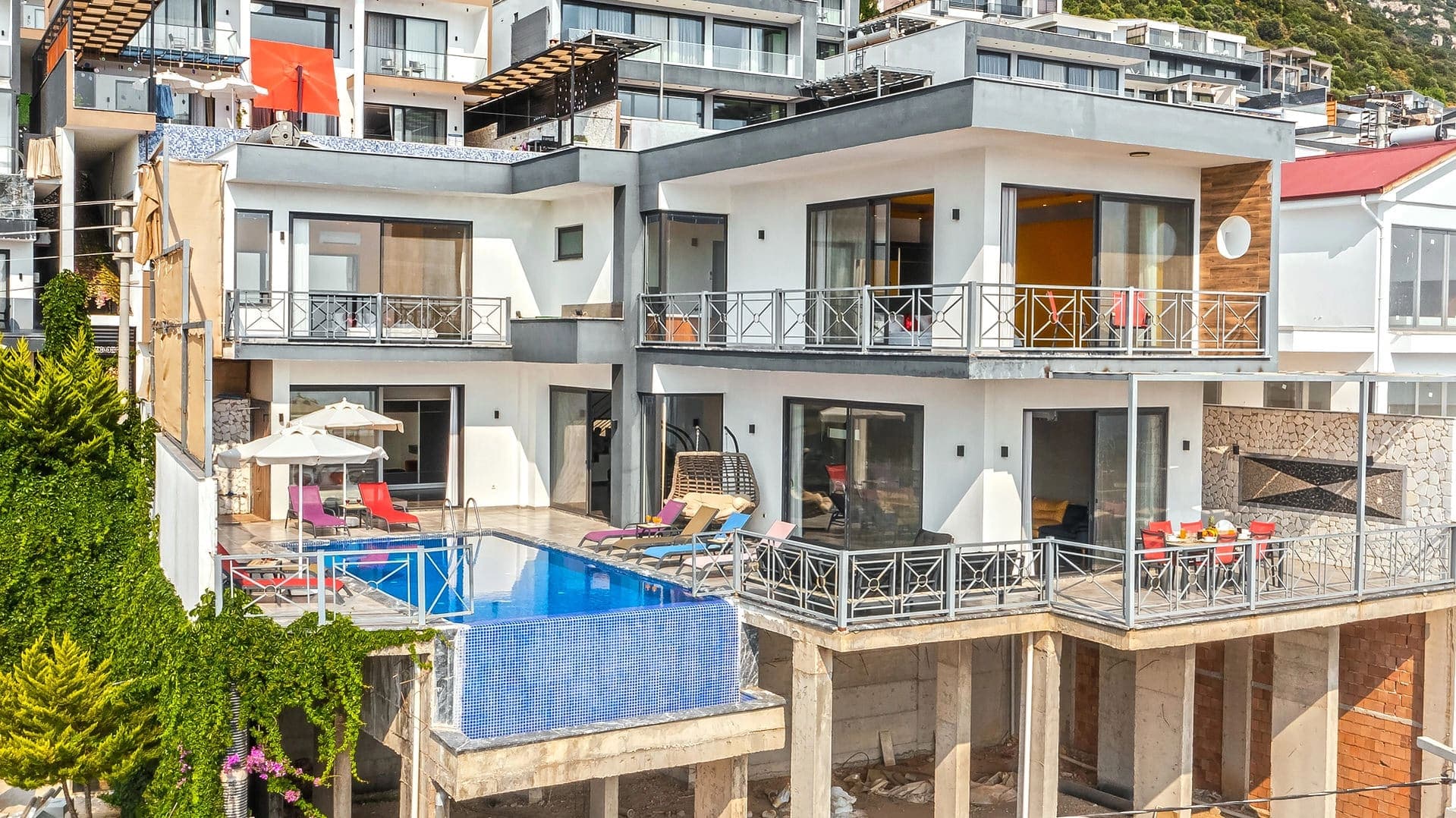 Dağ yamacında, havuzlu, beyaz ve gri tonlarda modern mimariye sahip çok katlı villa.