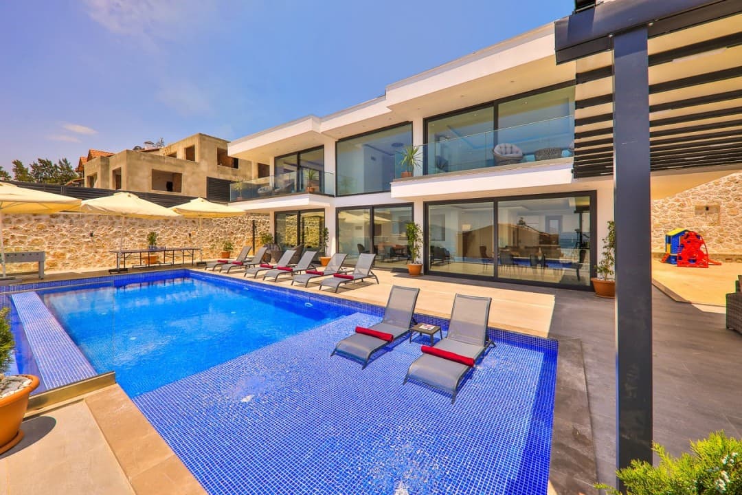 Gündüz vakti havuzunda şezlonglar olan iki katlı beyaz modern villa.