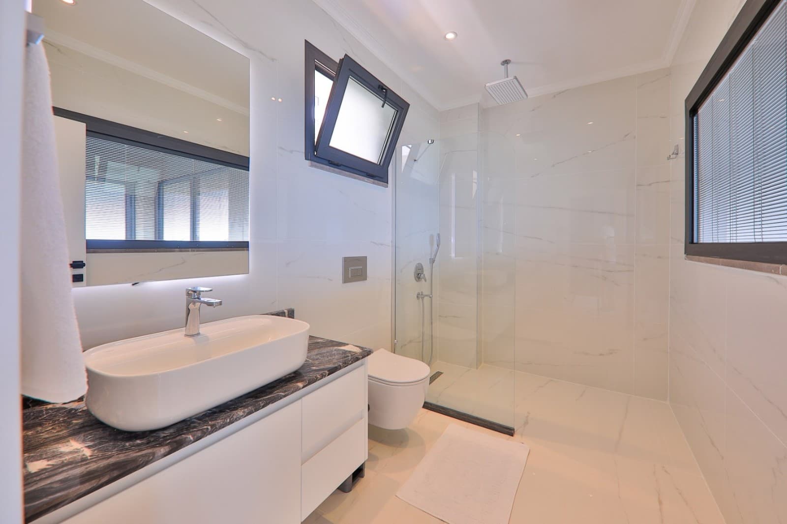 Beyaz mermer kaplı, cam duş kabinli ve LED aydınlatmalı aynalı modern banyo.