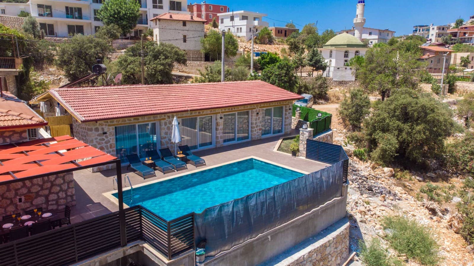 Kiremit çatılı taş villanın havuzu, şezlongları ve çevredeki köy evleri.