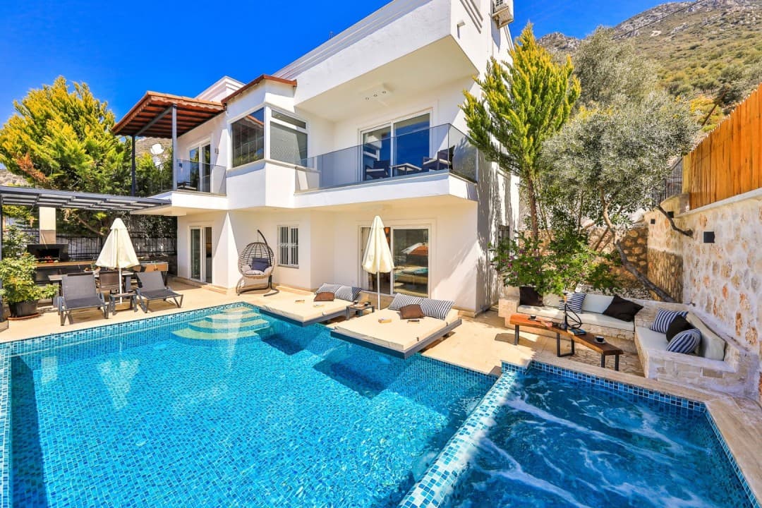 Jakuzili açık havuzu ve şezlongları olan beyaz dış cepheli villa.