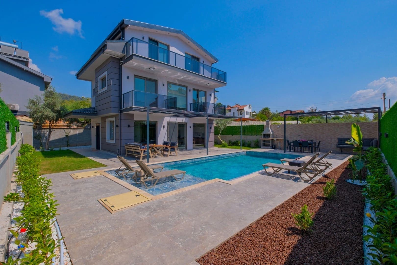 Önünde yüzme havuzu ve şezlonglar bulunan çok katlı modern villa