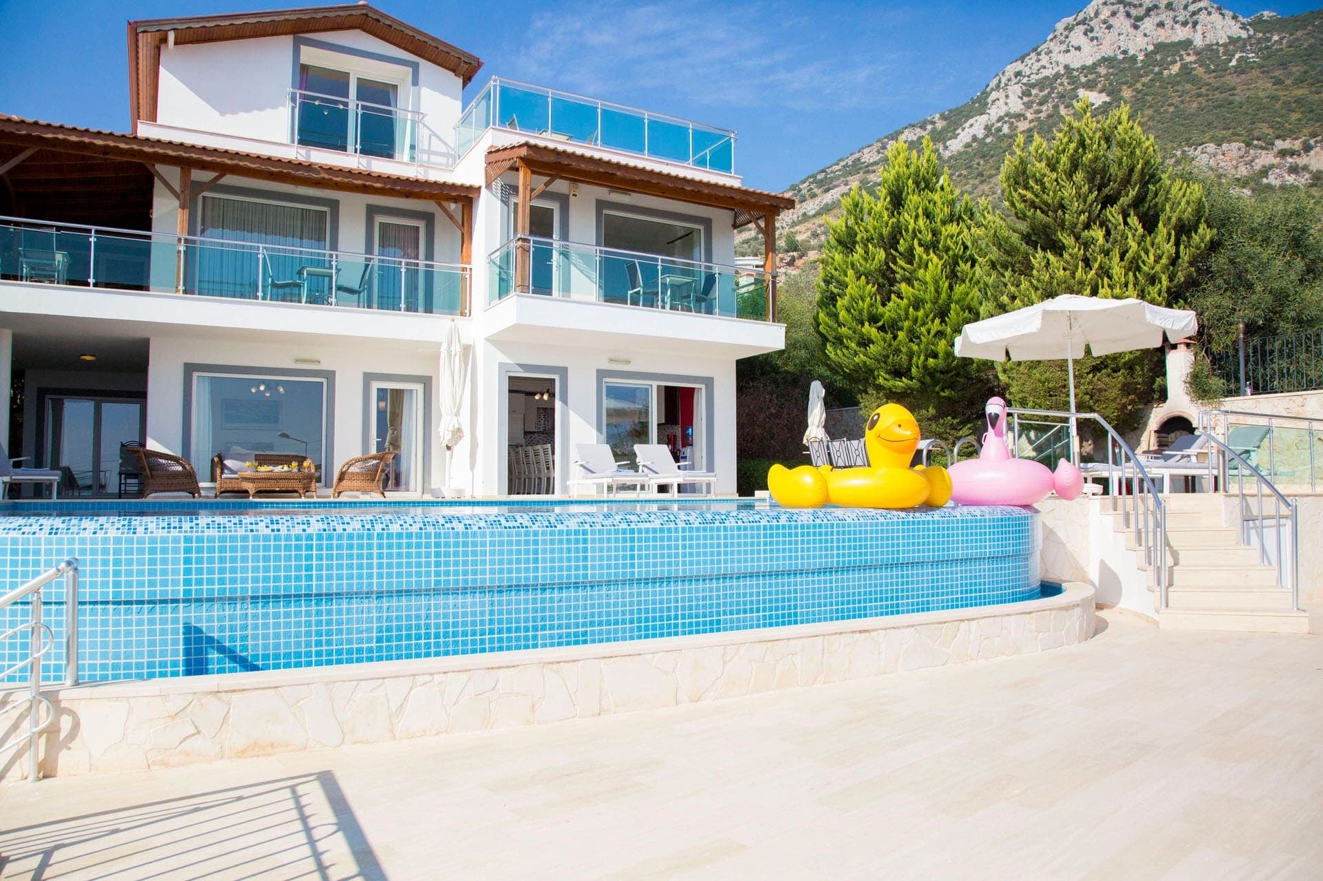 Havuz kenarında ördek ve flamingo şeklinde şişme yataklar bulunan villa dış cephesi.