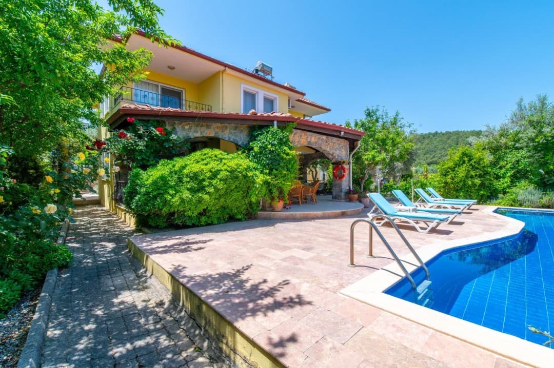 Taş kaplamalı verandası, özel havuzu ve şezlongları olan sarı renkli iki katlı müstakil villa.