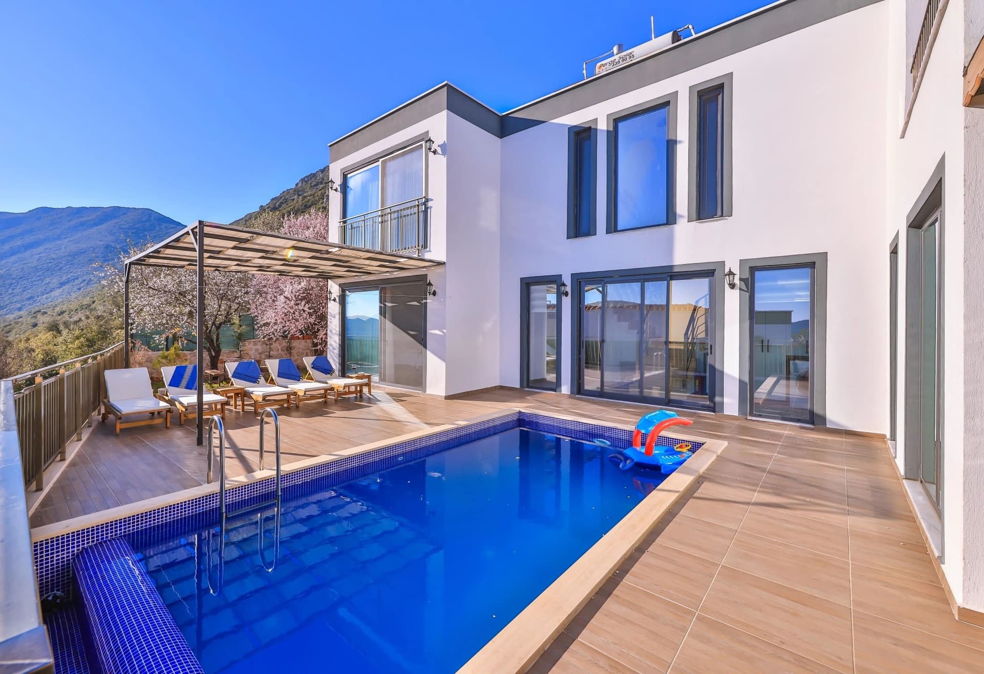 Mavi fayanslı havuzun yanında şezlonglar ve gölgelikli bir oturma alanı bulunan villa terası.