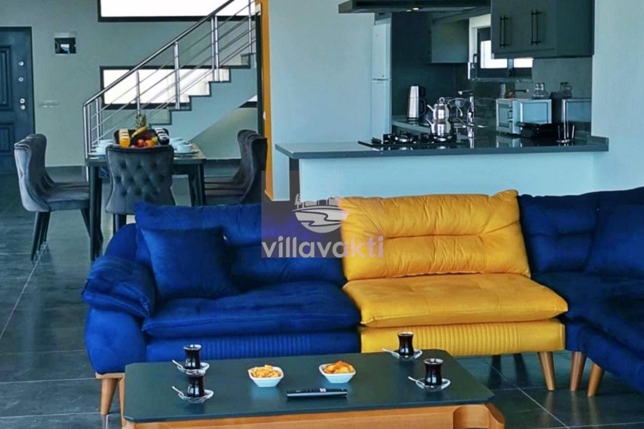 Mavi ve sarı koltuk takımı, yemek masası ve açık mutfağın olduğu modern bir salon.