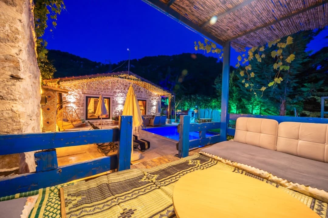 Akşam saatinde ışıklandırılmış taş evin önünde havuz ve veranda oturma alanı var.