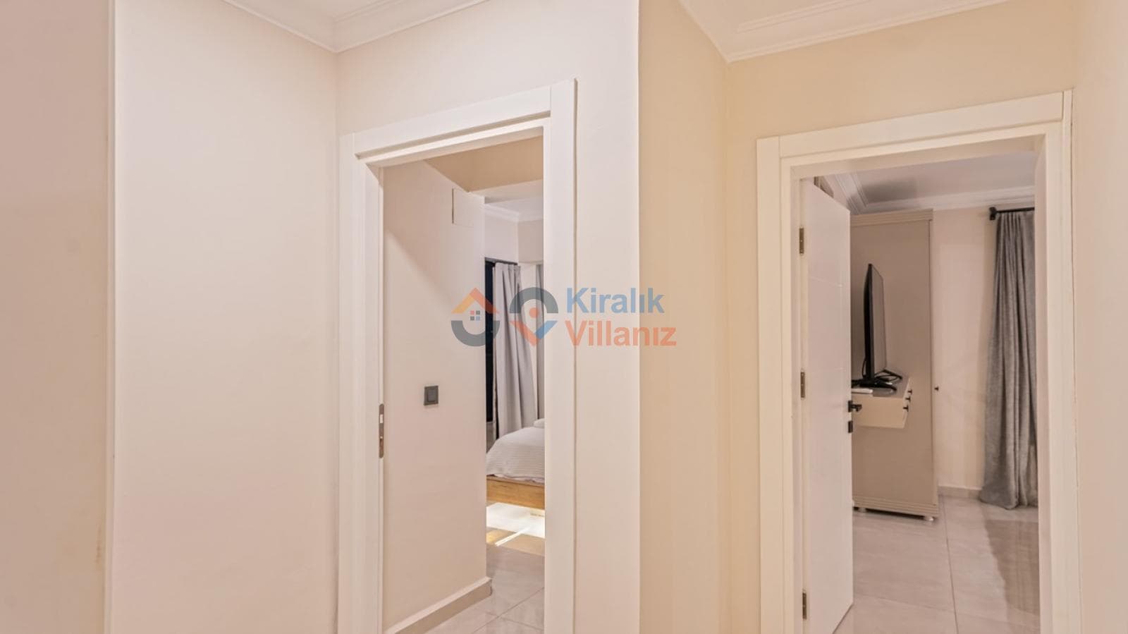 Beyaz duvarlı, açık renk zeminli, kapıları yatak odalarına açılan sade bir koridor.