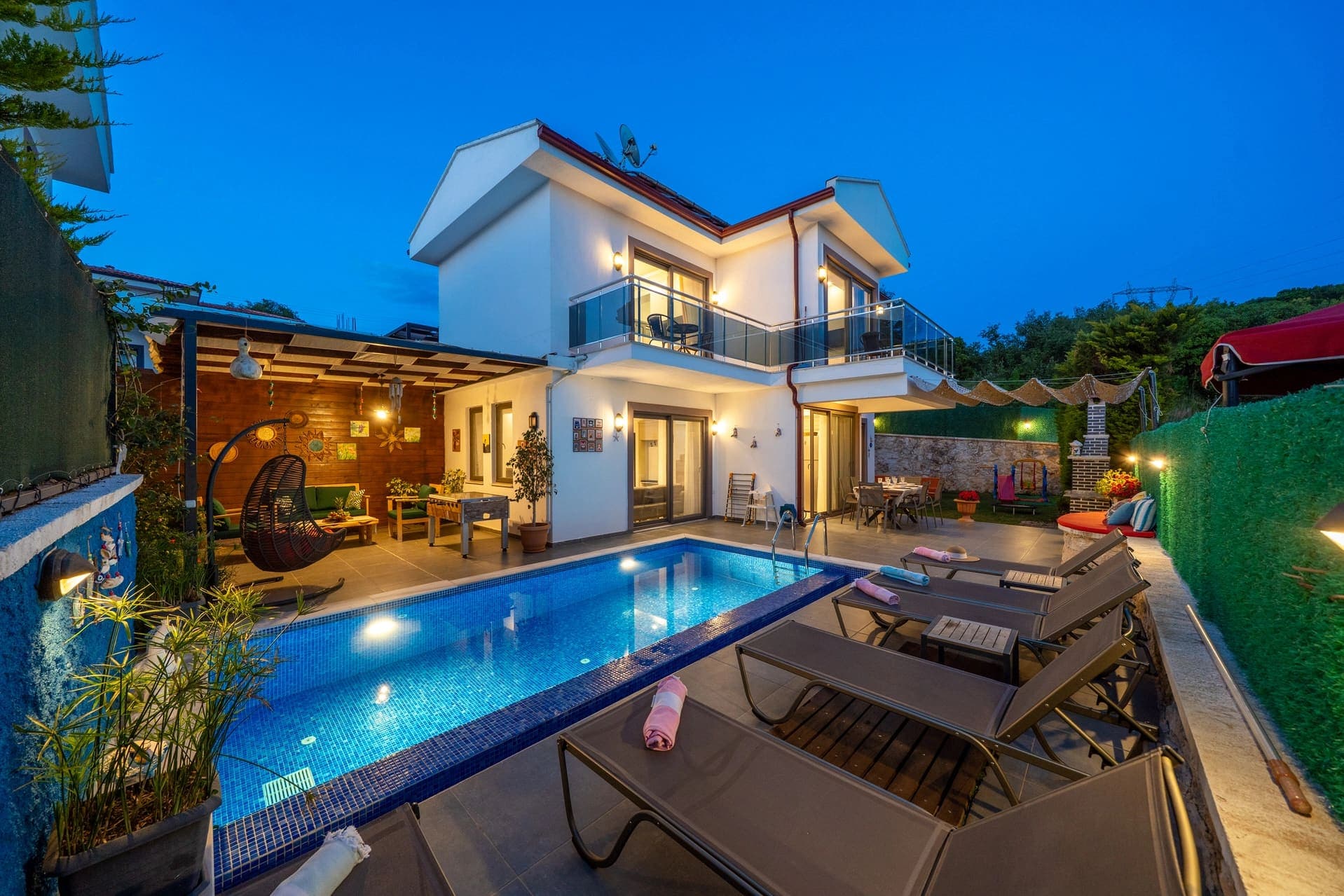 Akşam aydınlatmalı havuz kenarında şezlonglar ve iki katlı villa.