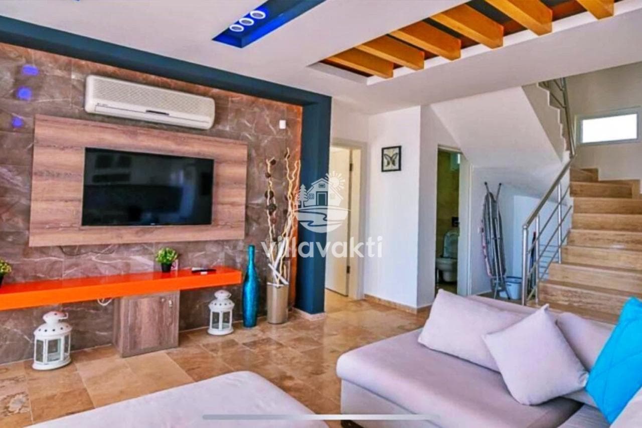 Turuncu raflı televizyon ünitesi, gri koltuk ve üst kata çıkan merdivenlerin olduğu salon.