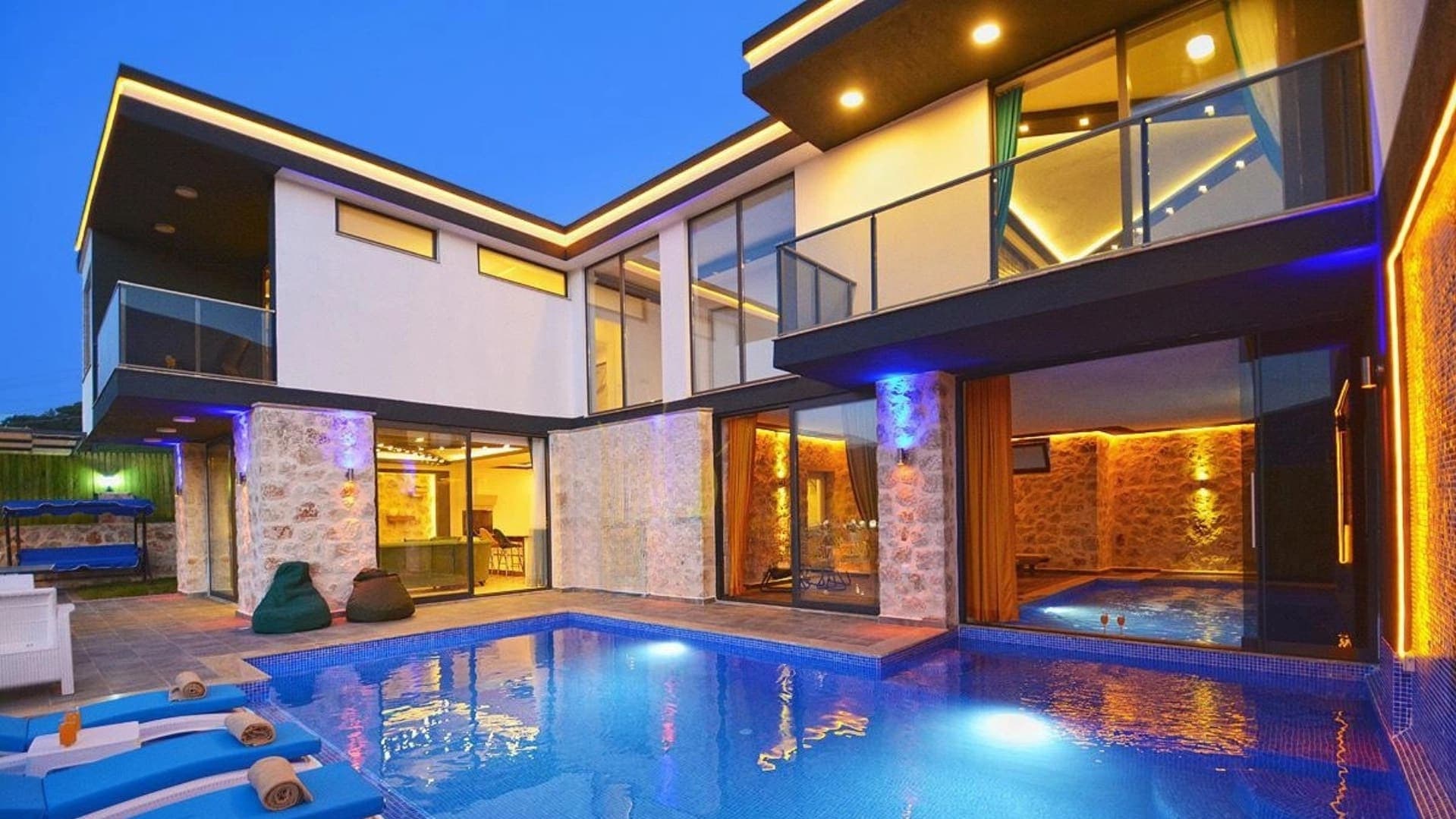 Gece aydınlatmalı havuzu ve balkonlu modern villanın dış cephesi.