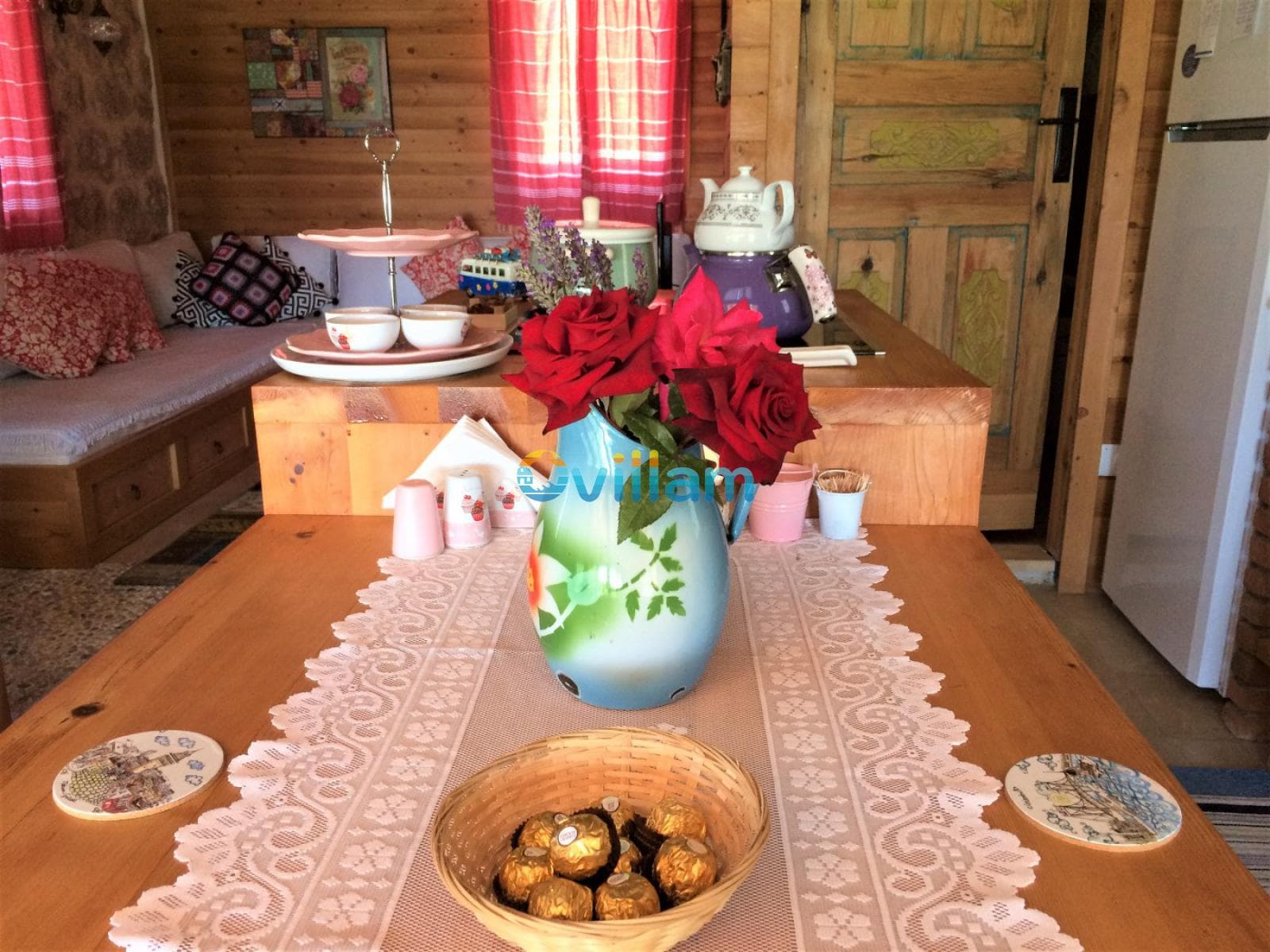Ahşap duvarlı odada, üzerinde kırmızı güller ve çikolata kasesi bulunan ahşap yemek masası.