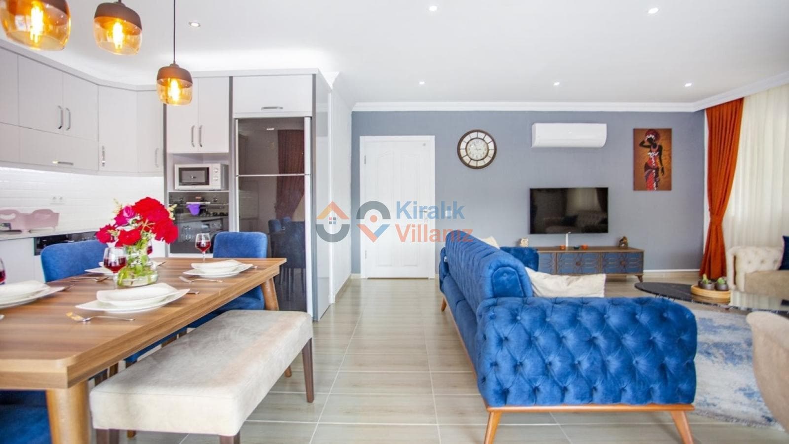 Mavi koltuk takımı, yemek masası ve açık mutfağın bulunduğu modern tasarımlı geniş bir salon.