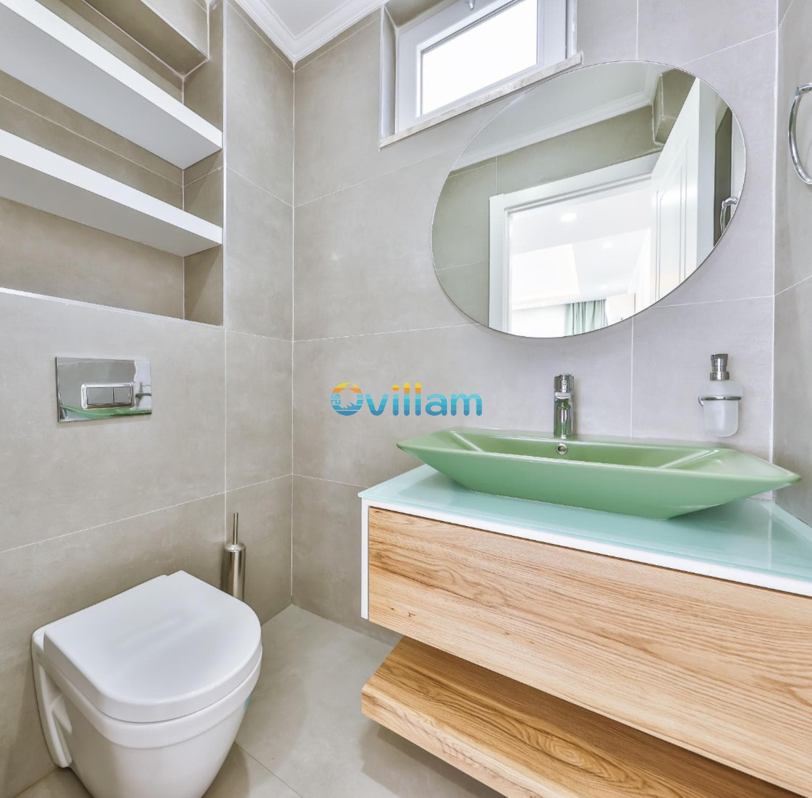 Bej fayanslı banyoda yeşil lavabo, ahşap dolap ve yuvarlak ayna yer alıyor.