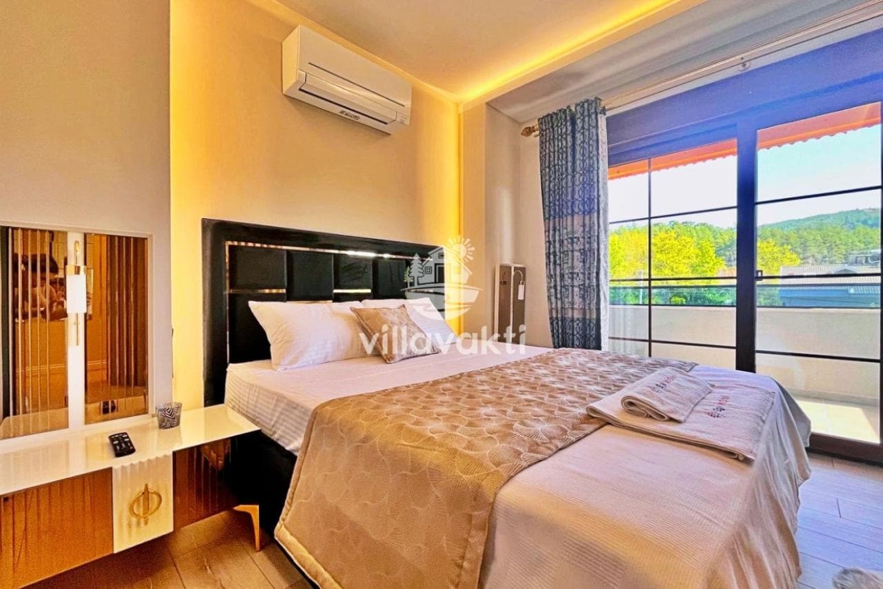 Çift kişilik yatak, modern başlık, aydınlatmalı tavan ve balkon kapısı bulunan yatak odası.