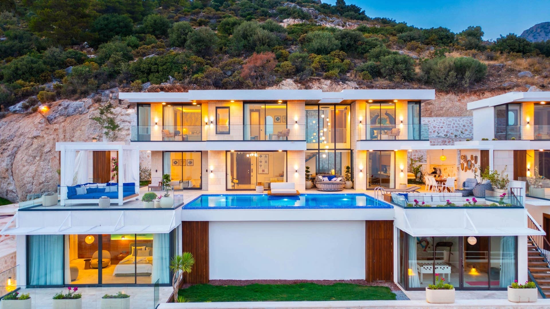 Dağ yamacında yer alan, önünde havuz ve geniş teras alanları bulunan iki katlı modern villa.